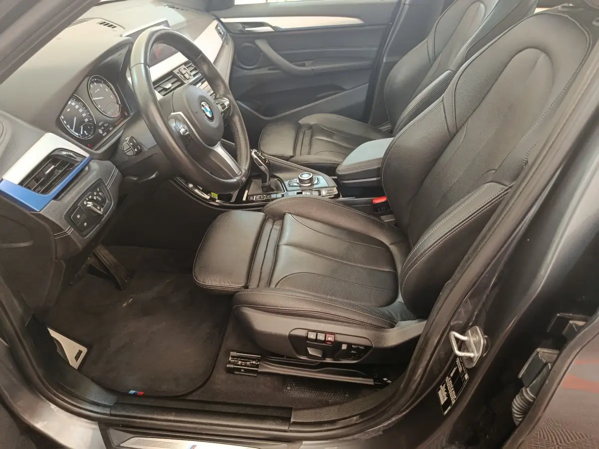 Intérieur avant droit d'une BMW X1 sDrive18i M Sport 2019 avec sièges cuir noirs et tableau de bord moderne.