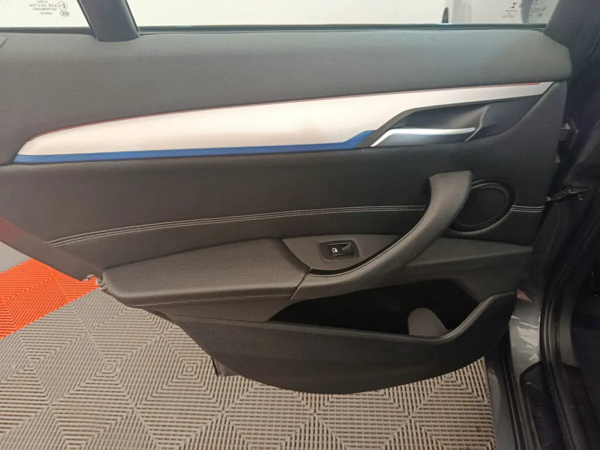 Vue intérieure côté gauche de la porte d'une BMW X1 sDrive18i M Sport 2019 avec garniture noire et insert blanc-bleu.