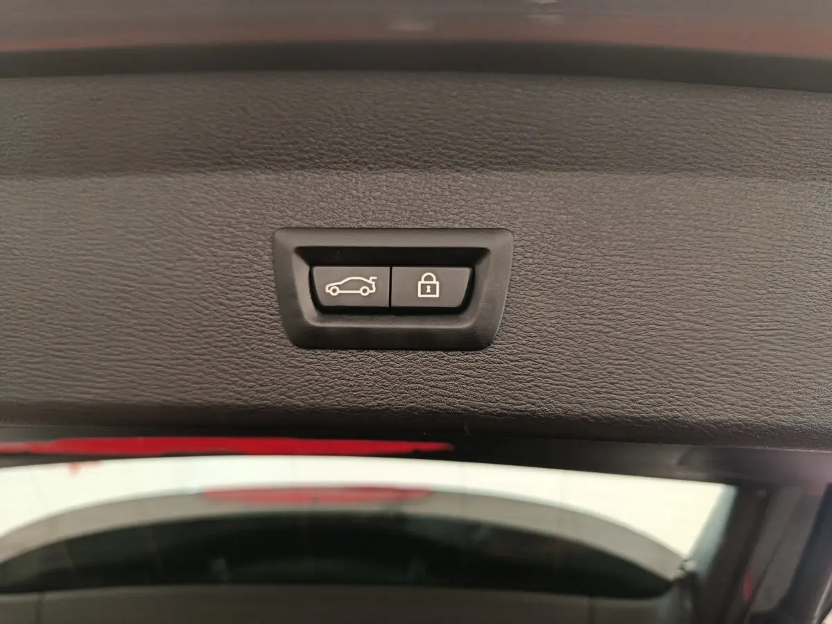 Gros plan sur les boutons d'ouverture et de verrouillage du coffre d'un BMW X1 sDrive18i M Sport 2019, intérieur noir.