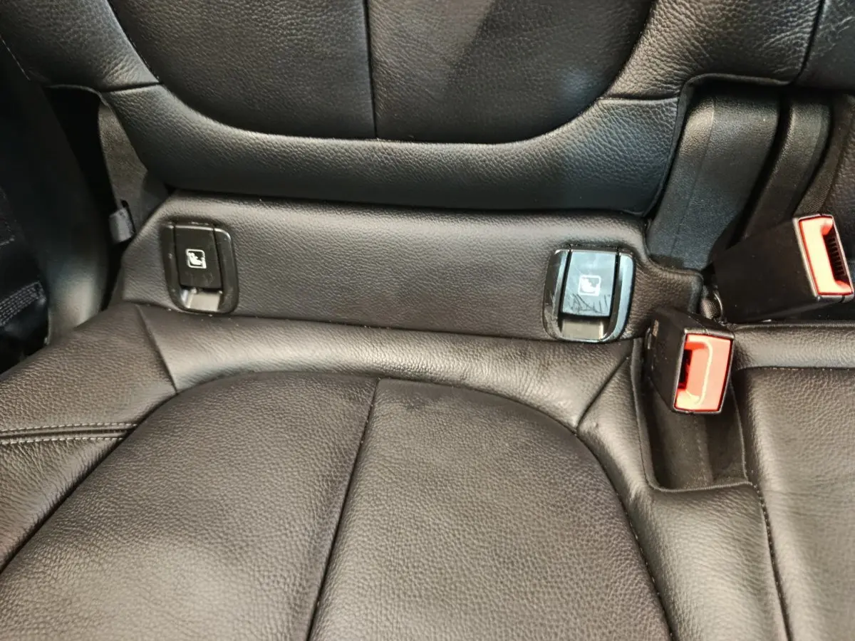 Gros plan sur la banquette arrière noire en cuir du BMW X1 sDrive18i M Sport, avec attaches Isofix et boucles de ceinture rouges.