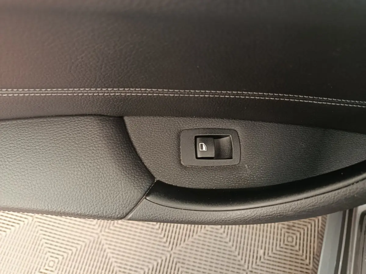 Bouton de commande de lève-vitre sur la porte intérieure côté conducteur d'une BMW X1 sDrive18i M Sport 2019, finition noire.