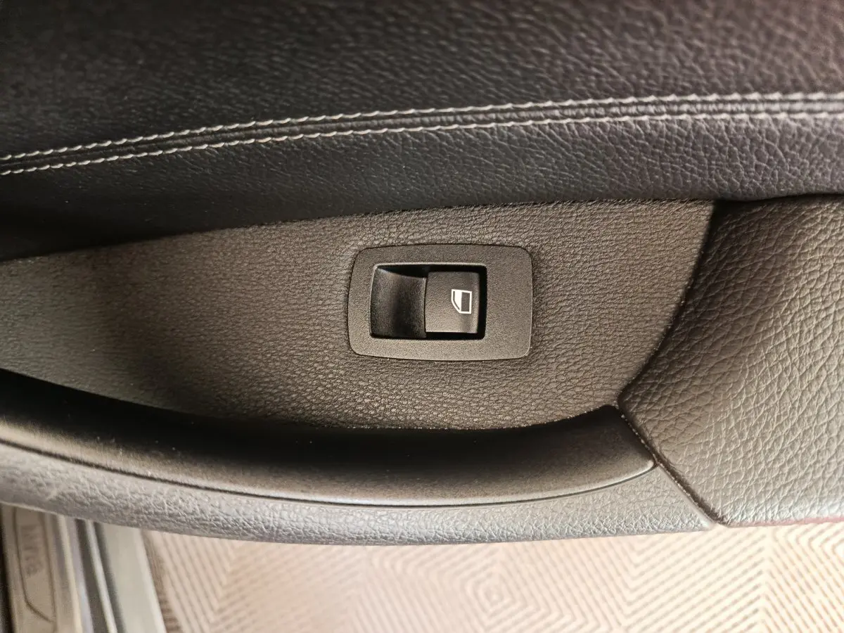 Gros plan sur le bouton de commande de lève-vitre en plastique noir sur la porte intérieure en cuir noir d'une BMW X1 sDrive18i M Sport 2019.