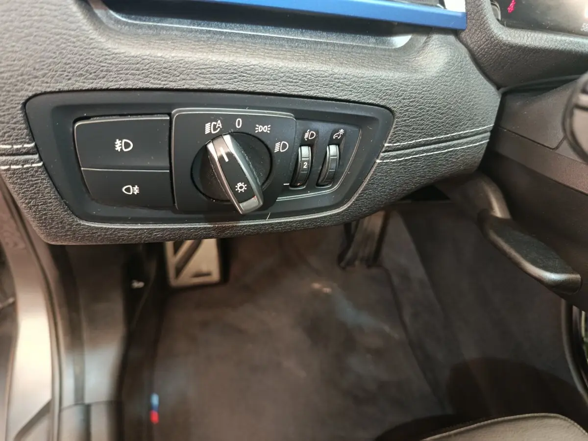 Gros plan sur le panneau de commande des phares à gauche du volant dans l'habitacle noir du BMW X1 sDrive18i M Sport 2019.