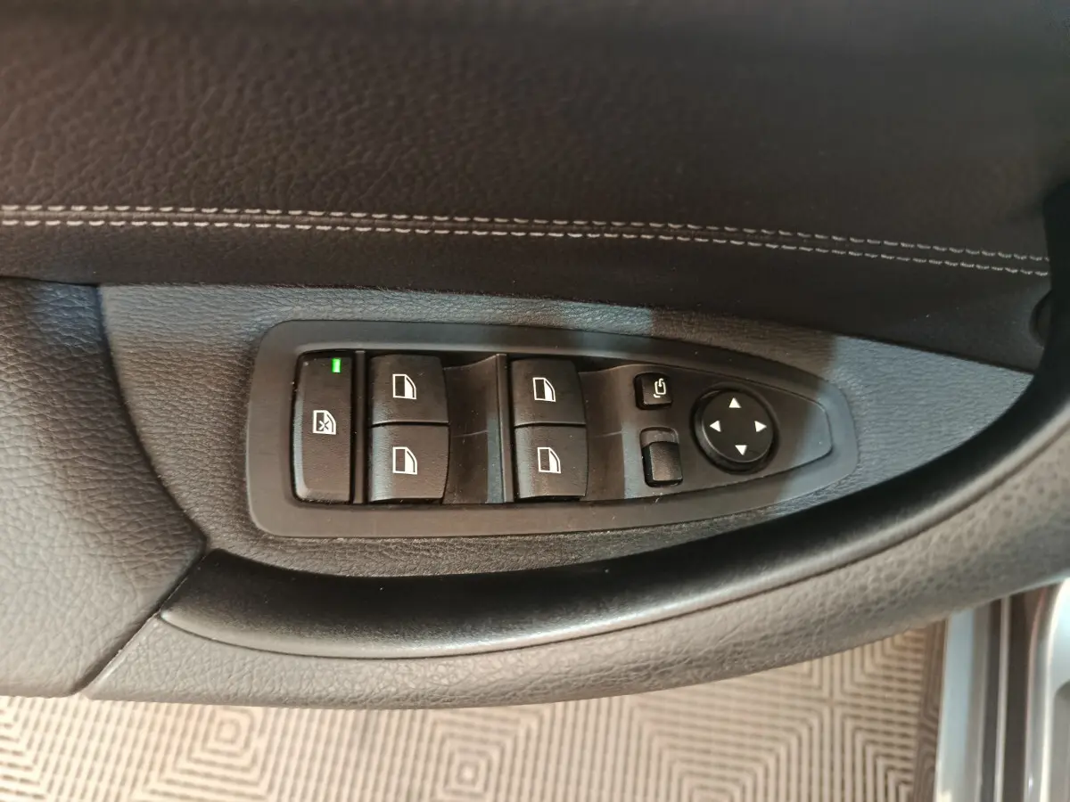 Gros plan sur les commandes de lève-vitres et rétroviseurs côté gauche d'une BMW X1 2019 finition M Sport.