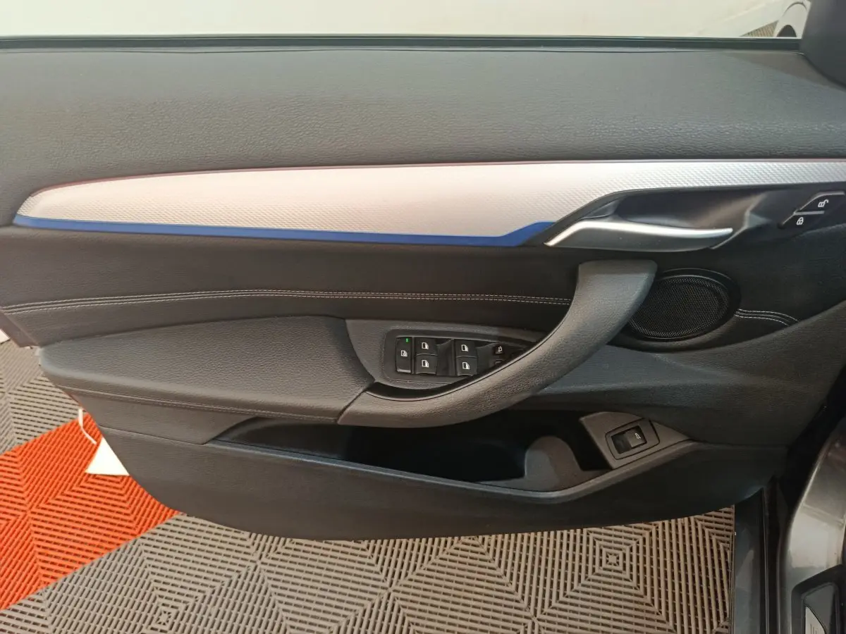 Vue intérieure côté gauche de la porte BMW X1 sDrive18i M Sport avec garniture noire et insert clair, commandes fenêtres visibles.