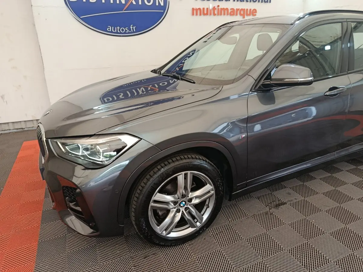 Vue 3/4 avant droit d'un BMW X1 sDrive18i M Sport gris métallisé avec jantes alliage et phares LED allumés.