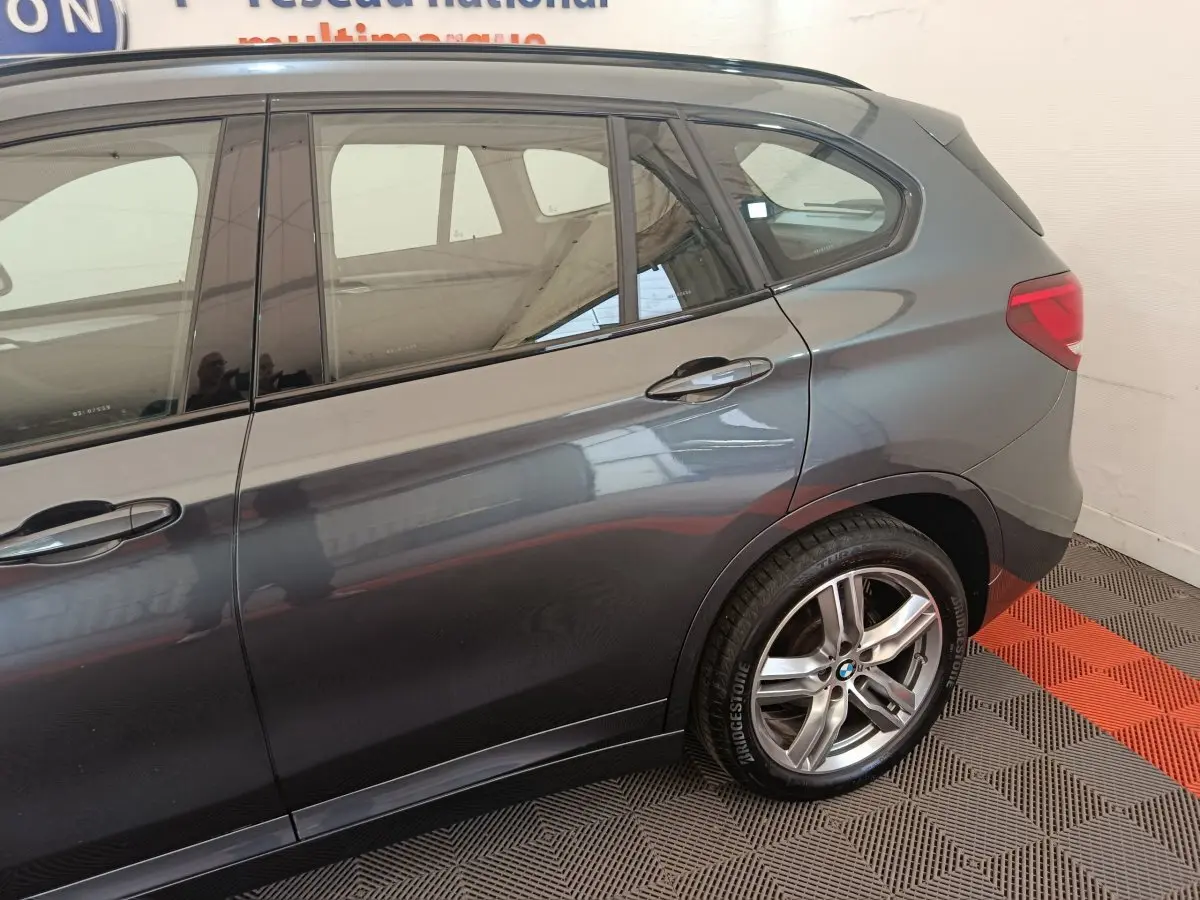 Vue latérale droite sur l'arrière d'un BMW X1 gris métallisé avec jantes alliage et feux arrière visibles.