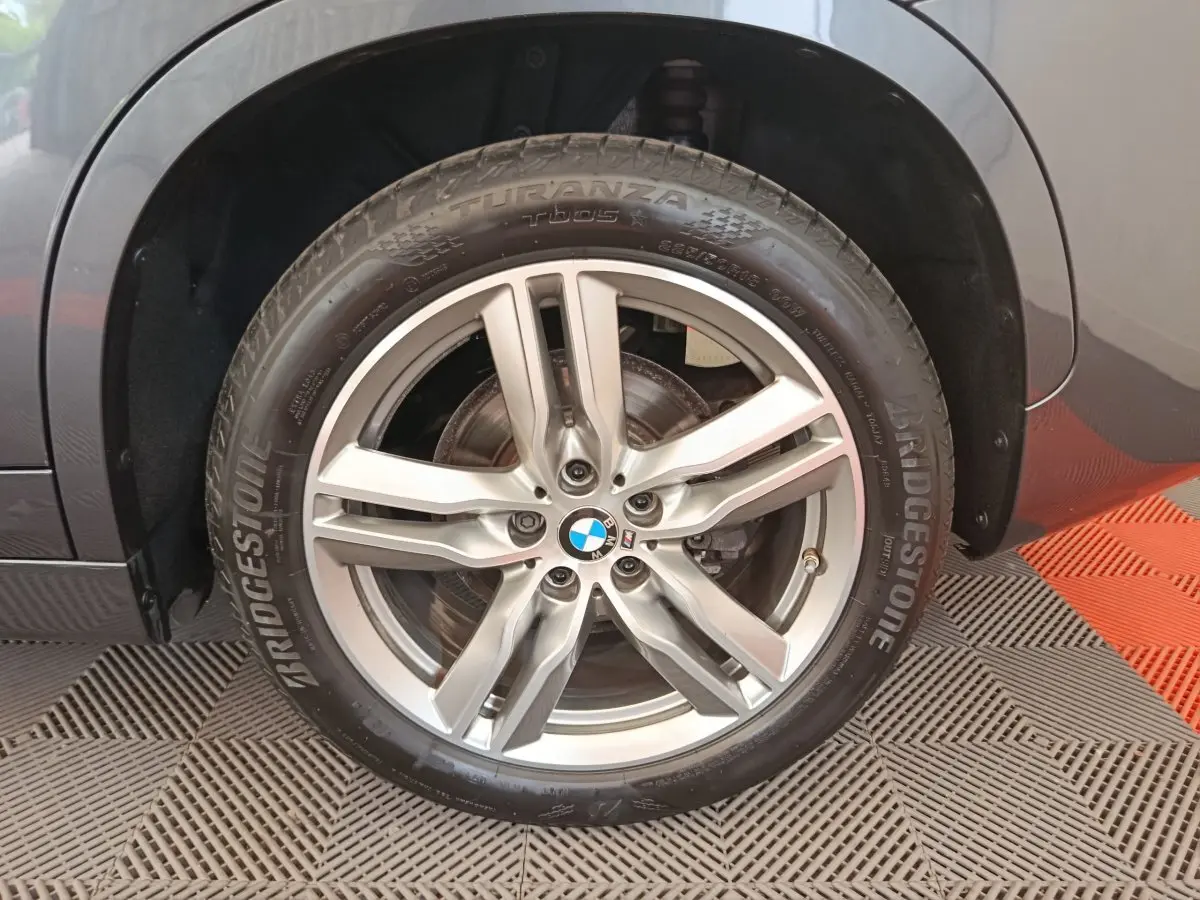 Gros plan sur la roue avant droite grise d'un BMW X1 sDrive18i M Sport avec jante alliage cinq branches.