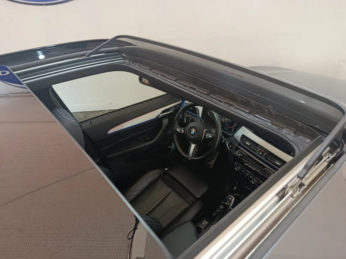 Vue plongeante sur l'intérieur noir d'une BMW X1 sDrive18i M Sport 2019 avec toit ouvrant panoramique ouvert.