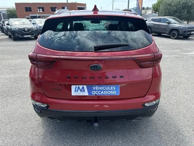 Vue arrière d'un Kia Sportage rouge métallisé 2021 avec logo et plaque d'occasion sur parking extérieur.