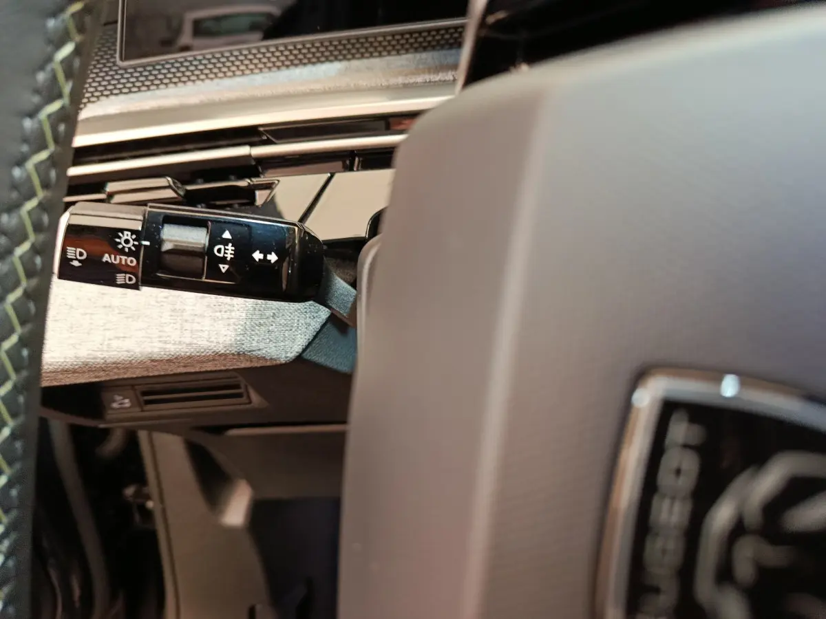 Gros plan sur la manette des feux à gauche du volant gris clair du Peugeot 3008 blanc hybride 2025.