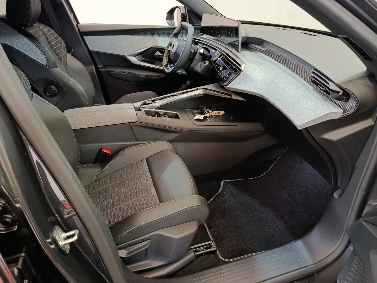 Intérieur côté conducteur du Peugeot 3008 hybride 2025, tableau de bord moderne avec écran tactile et sièges noirs et gris.