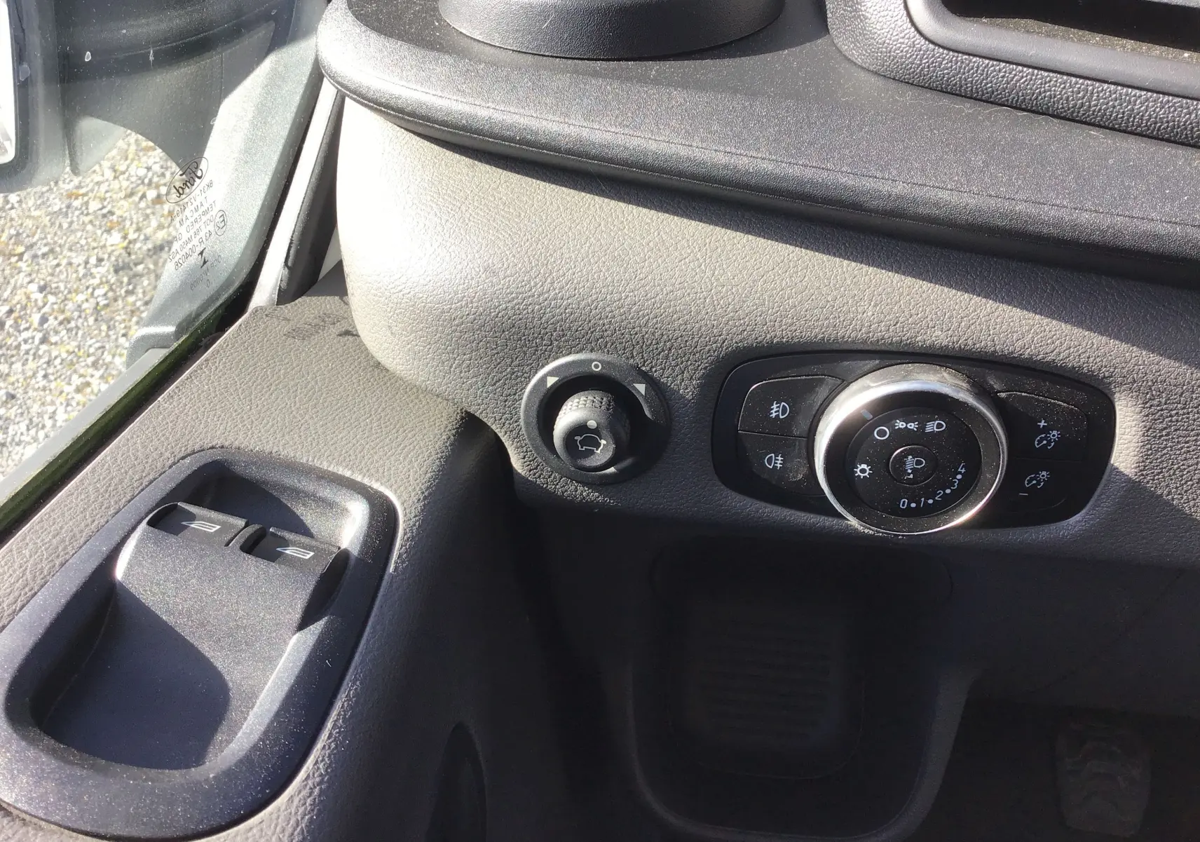 Détail intérieur côté gauche du tableau de bord du Ford Transit blanc, avec commandes d'éclairage et boutons de vitres électriques.