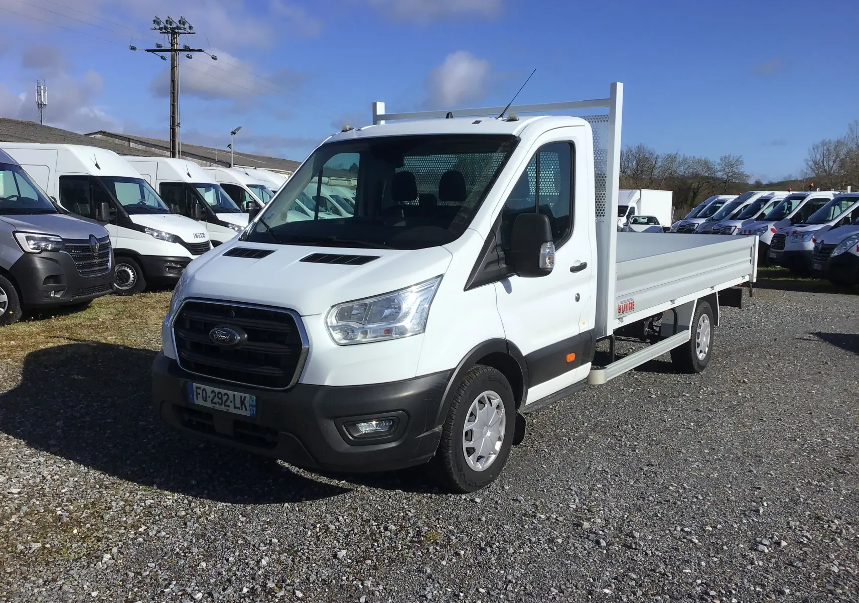Ford Transit Chassis Cabine blanc en 3/4 avant droit, avec plateau 4 mètres et ridelles en aluminium visibles.
