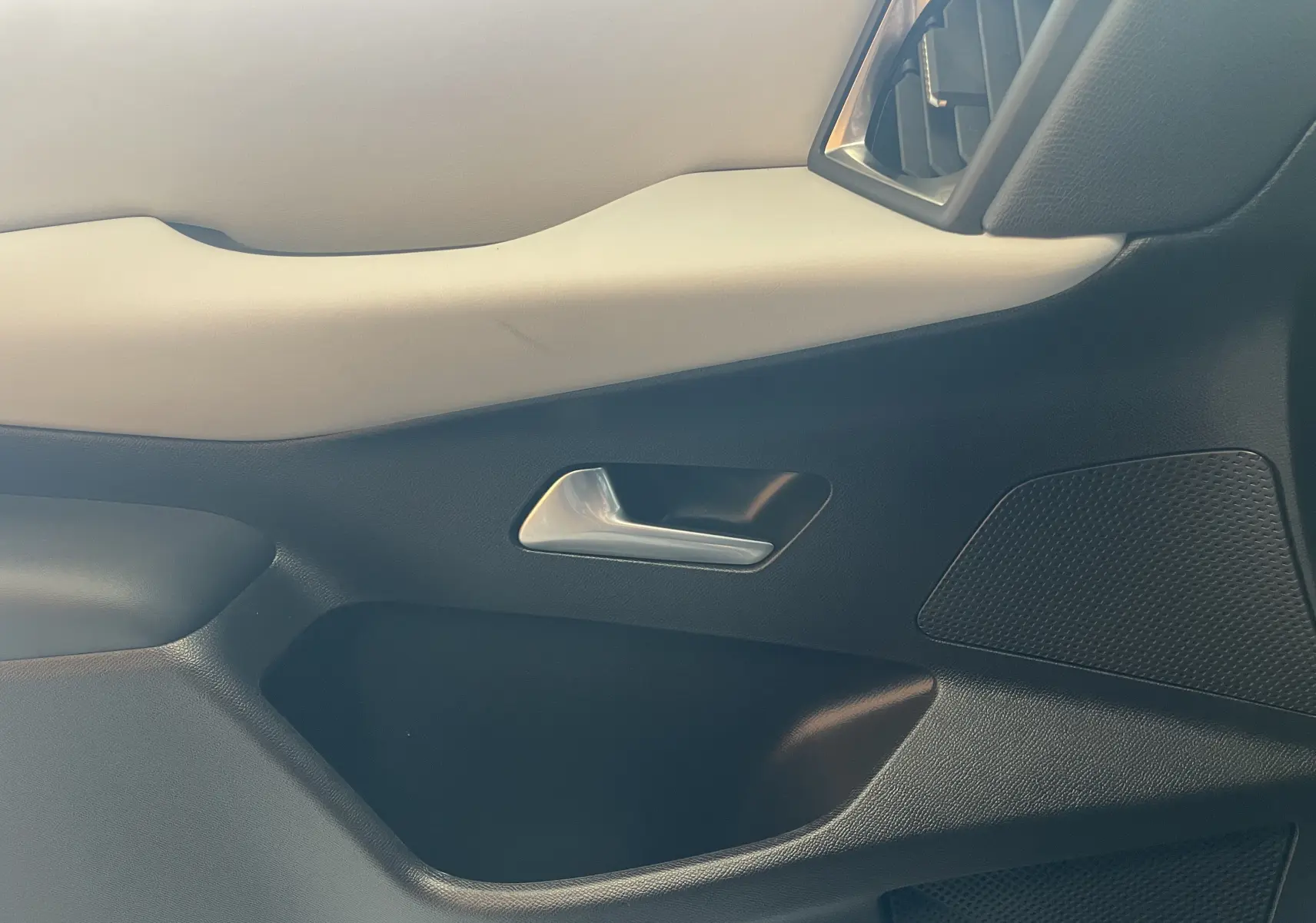 Gros plan sur la garniture intérieure côté droit du DS3 Crossback 2024, avec poignée argentée et panneau bicolore noir et beige.