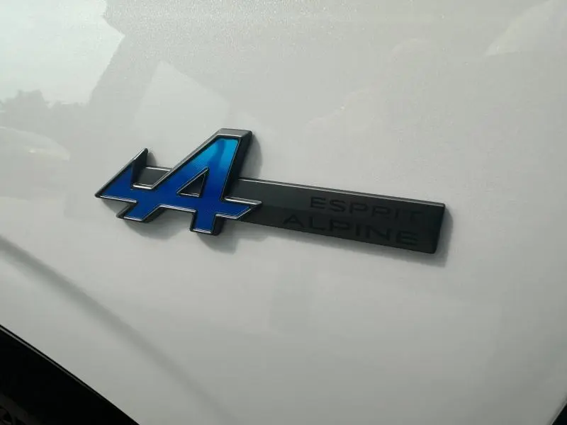 Gros plan sur l'emblème bleu Esprit Alpine du Renault Austral gris, soulignant la finition sportive du modèle hybride.