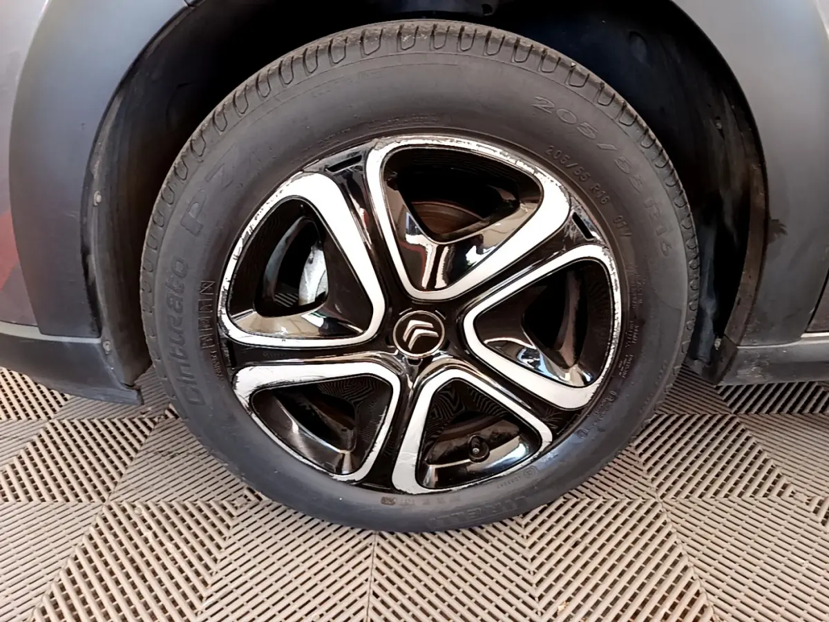 Gros plan sur la roue avant gauche d'une Citroën C3 gris foncé, mettant en valeur la jante noire et chromée au design moderne.