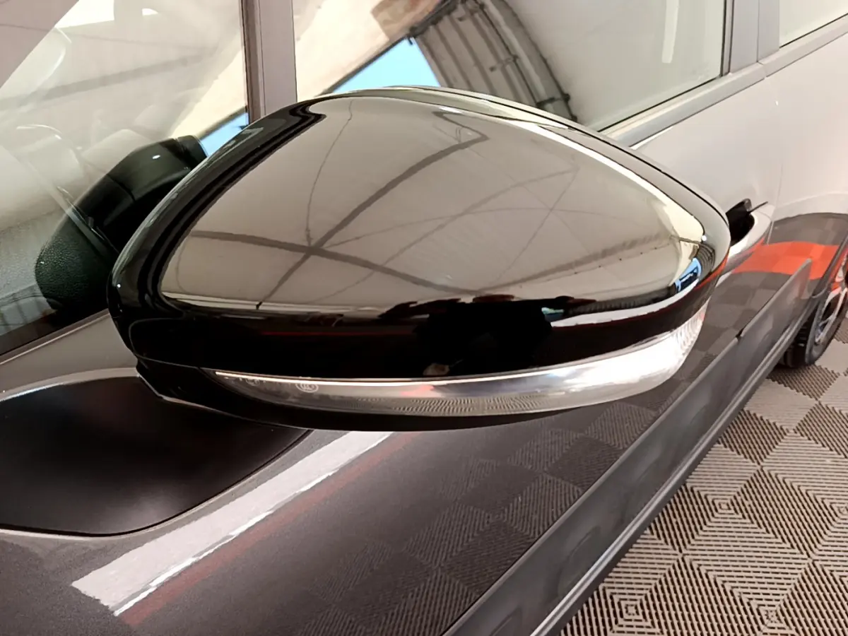 Rétroviseur noir brillant côté conducteur d'une Citroën C3 gris foncé vue de près sur fond intérieur.