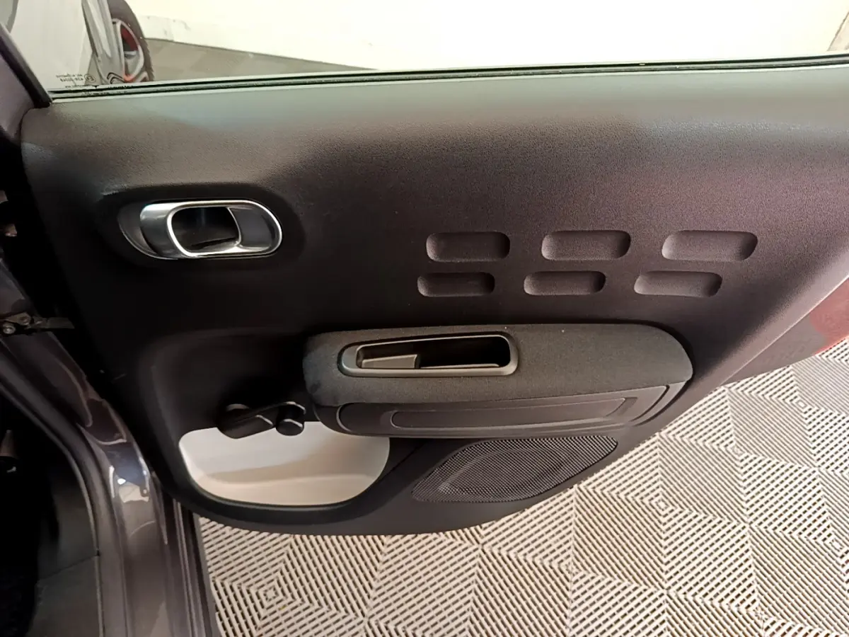 Détail de la porte côté gauche de la Citroën C3 gris foncé avec poignée intérieure et commandes manuelles.
