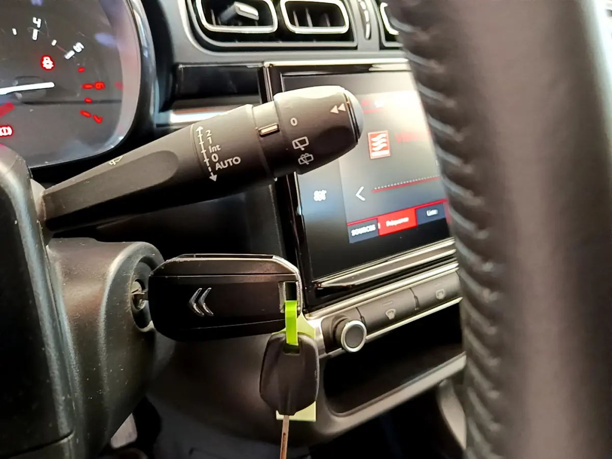 Gros plan sur le volant et le commodo gauche de la Citroën C3 gris foncé, avec clé insérée et écran tactile visible.