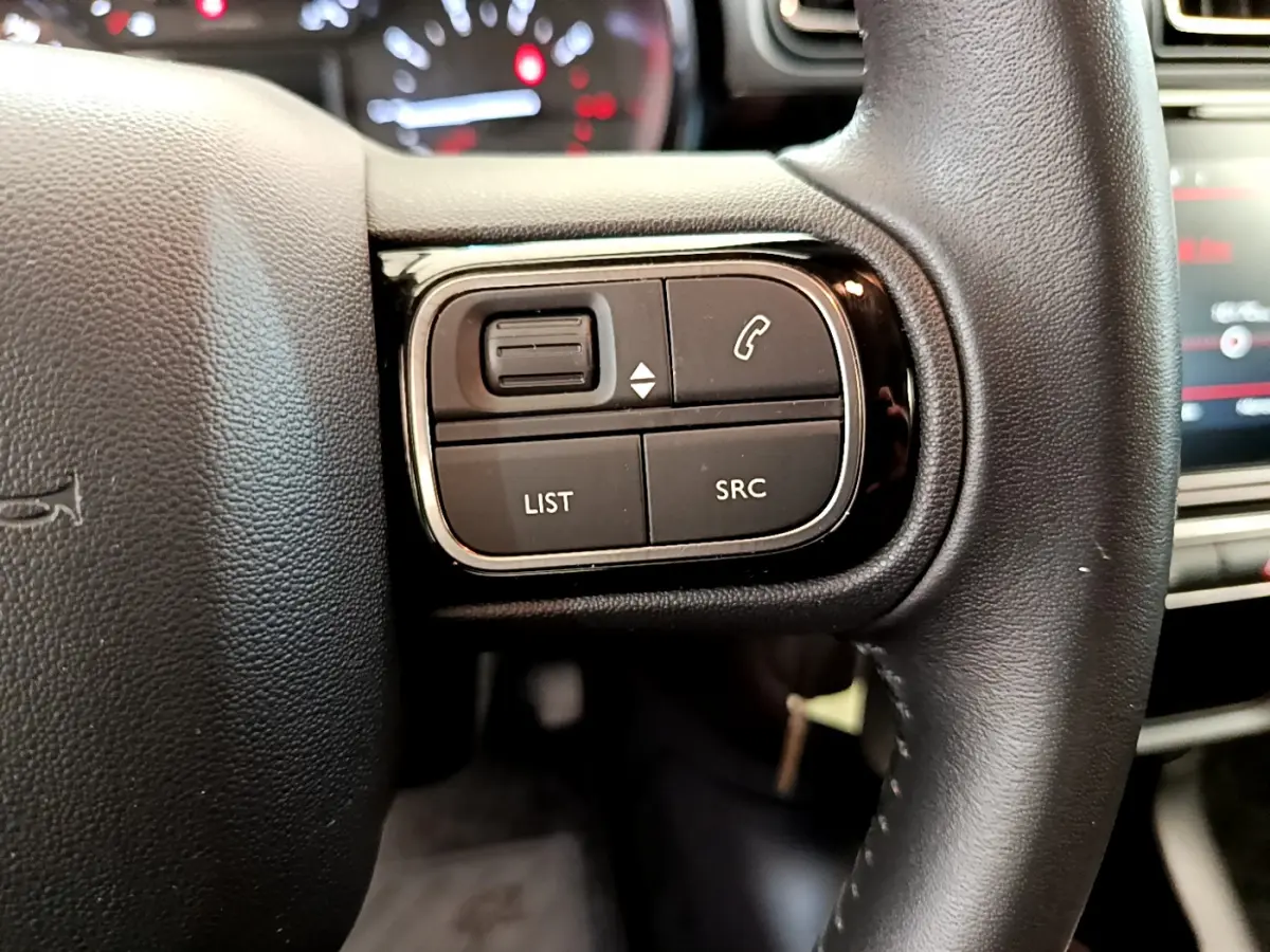 Gros plan sur les commandes gauche du volant cuir noir de la Citroën C3 gris foncé, avec boutons de téléphone et audio.