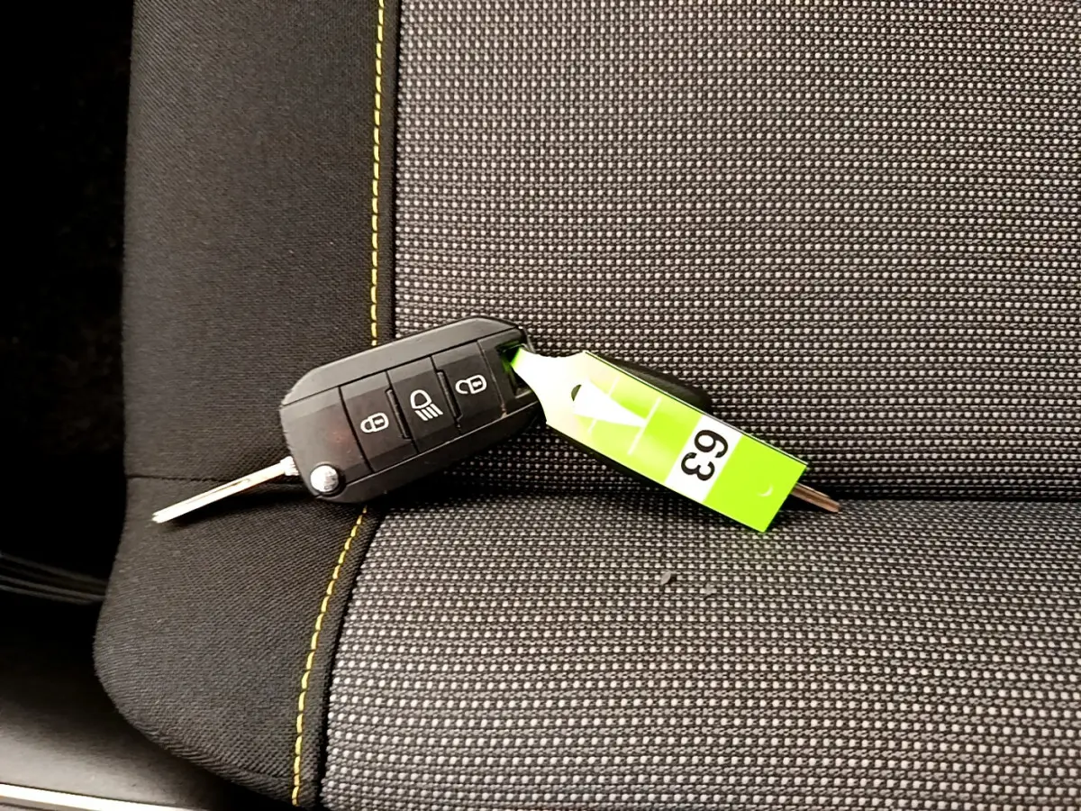 Clé de contact noire posée sur un siège avant gris foncé à surpiqûres jaunes d'une Citroën C3 PureTech 2019.