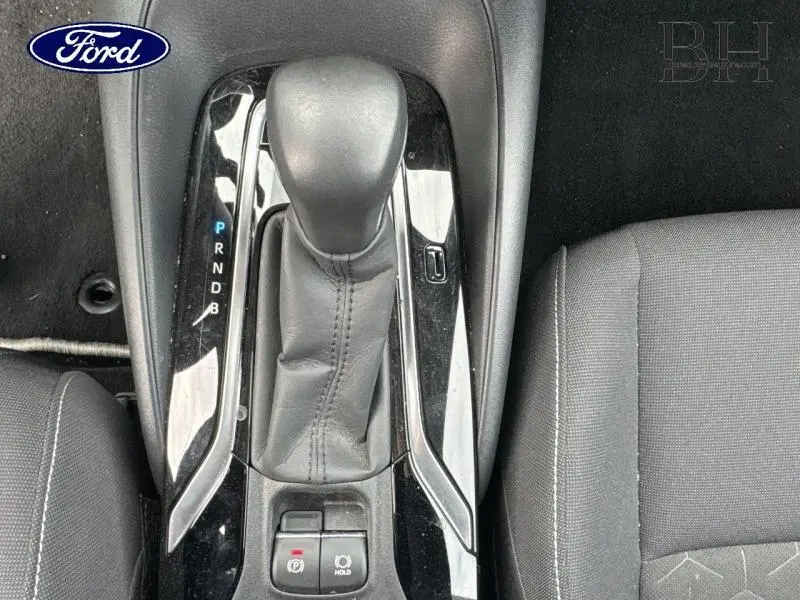 Le levier de vitesses automatique noir et cuir de la Toyota Corolla 122h Dynamic Business vu de dessus avec siège tissu noir adjacent.