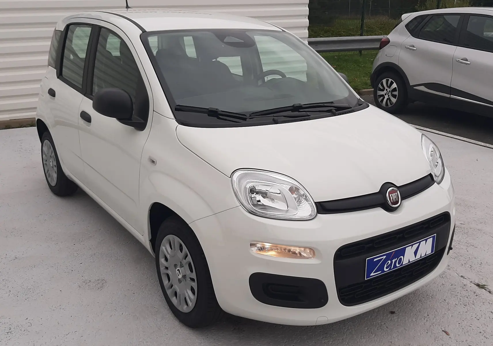 Vue 3/4 avant d'une Fiat Panda blanche Gelato 2025 avec cinq portes, dans un parking extérieur.