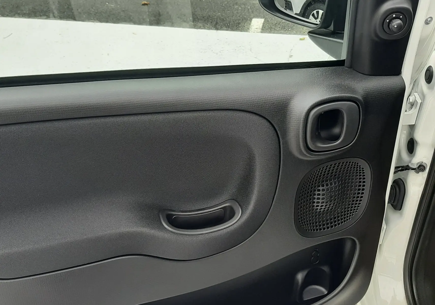 Intérieur de la porte avant gauche d'une Fiat Panda blanche, avec poignée intégrée et haut-parleur visible.