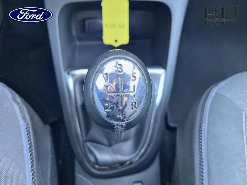 Le levier de vitesses manuel vu de dessus avec marquages des rapports, entouré de sièges en tissu gris.