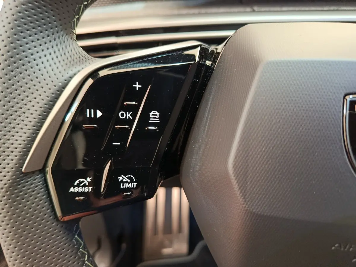 Gros plan sur les commandes multifonctions à gauche du volant perforé du Peugeot 3008 noir hybride 2025.