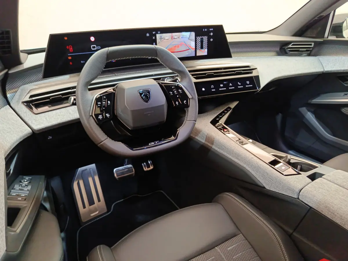 Intérieur moderne du Peugeot 3008 GT 2025, vue cockpit avec volant cuir, écran tactile large et console centrale grise.
