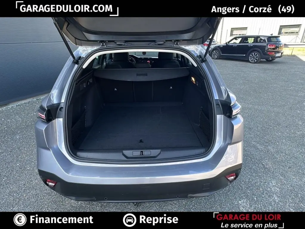 Vue arrière ouverte du coffre d'une Peugeot 308 gris clair 2023, montrant l'espace de chargement vide et le hayon levé.