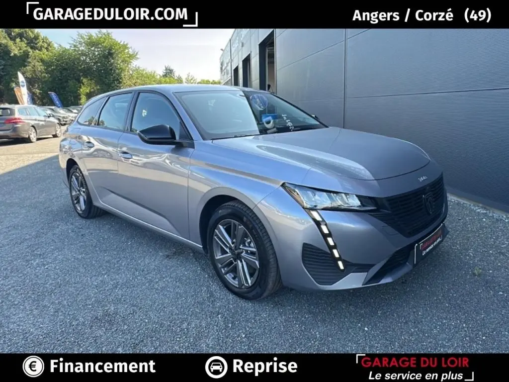 Peugeot 308 gris clair vue 3/4 avant droit, avec feux LED verticaux et jantes alliage distinctives.