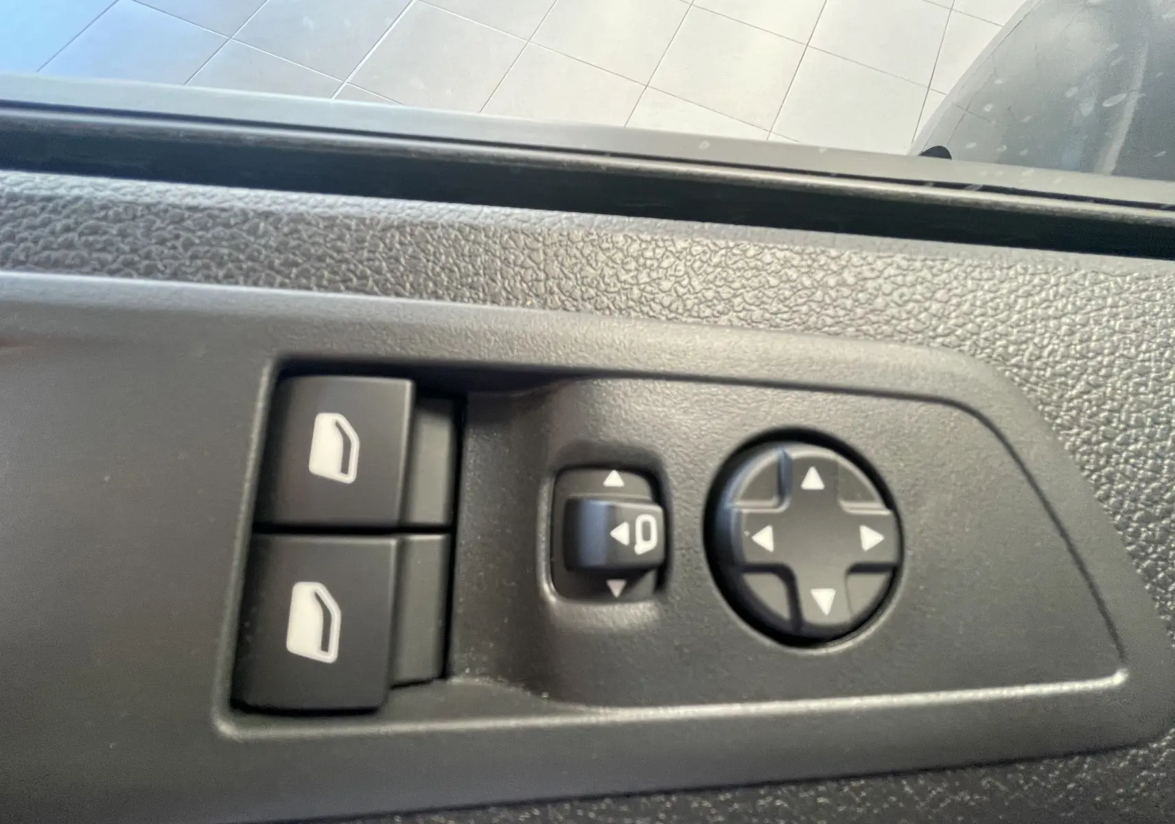 Gros plan sur les commandes de réglage des vitres et des rétroviseurs côté gauche du Peugeot Traveller noir 2026.