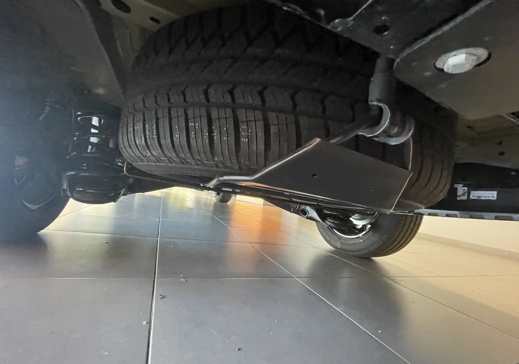 Vue en contre-plongée sous un Peugeot Traveller noir 2026, montrant la roue de secours et la suspension arrière.