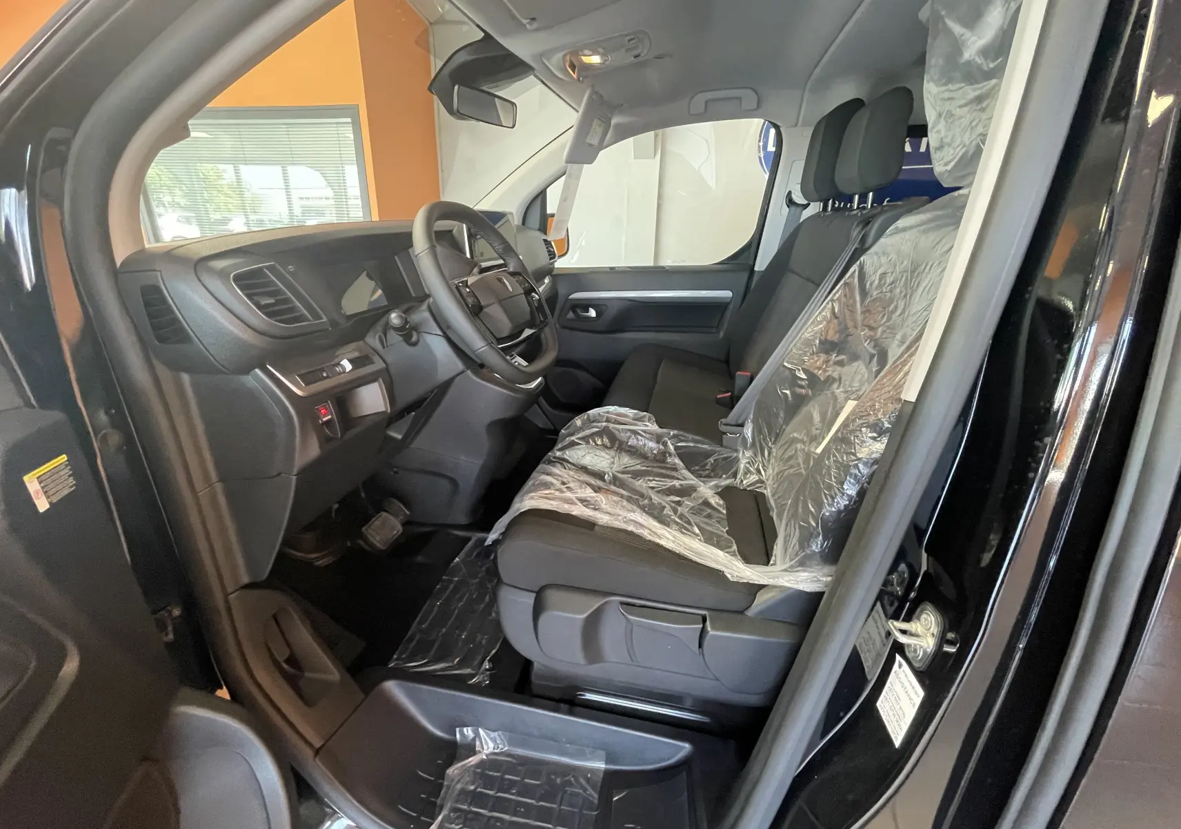 Intérieur avant droit du Peugeot Traveller noir 2026, montrant les sièges plastifiés et le tableau de bord moderne.