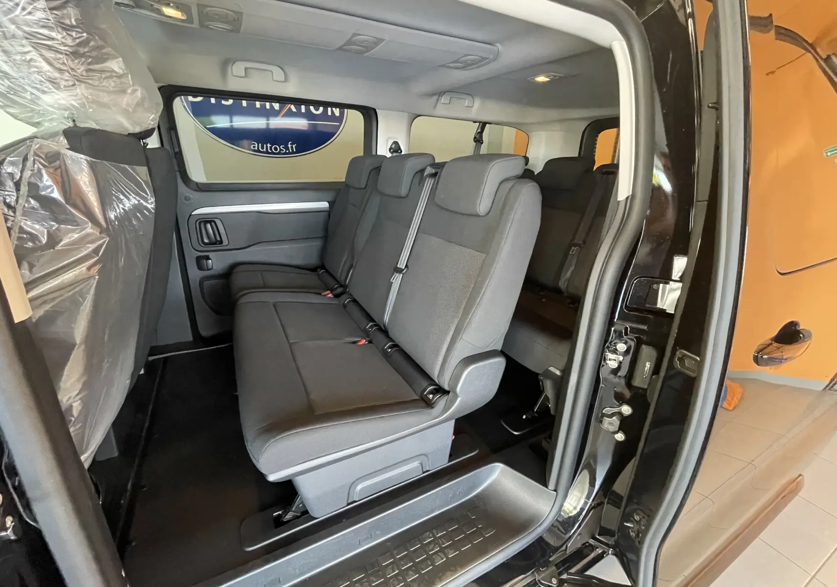 Vue intérieure côté droit du Peugeot Traveller noir 2026, montrant les sièges arrière en tissu gris et la porte coulissante ouverte.