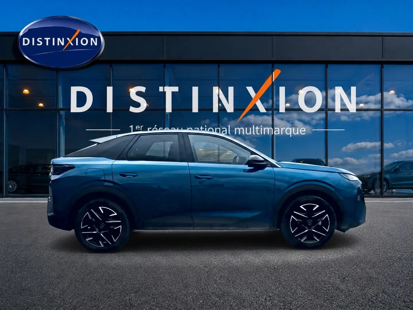 Profil côté gauche d’un Peugeot 3008 bleu 2025 avec jantes alu noires et toit noir devant un bâtiment vitré.