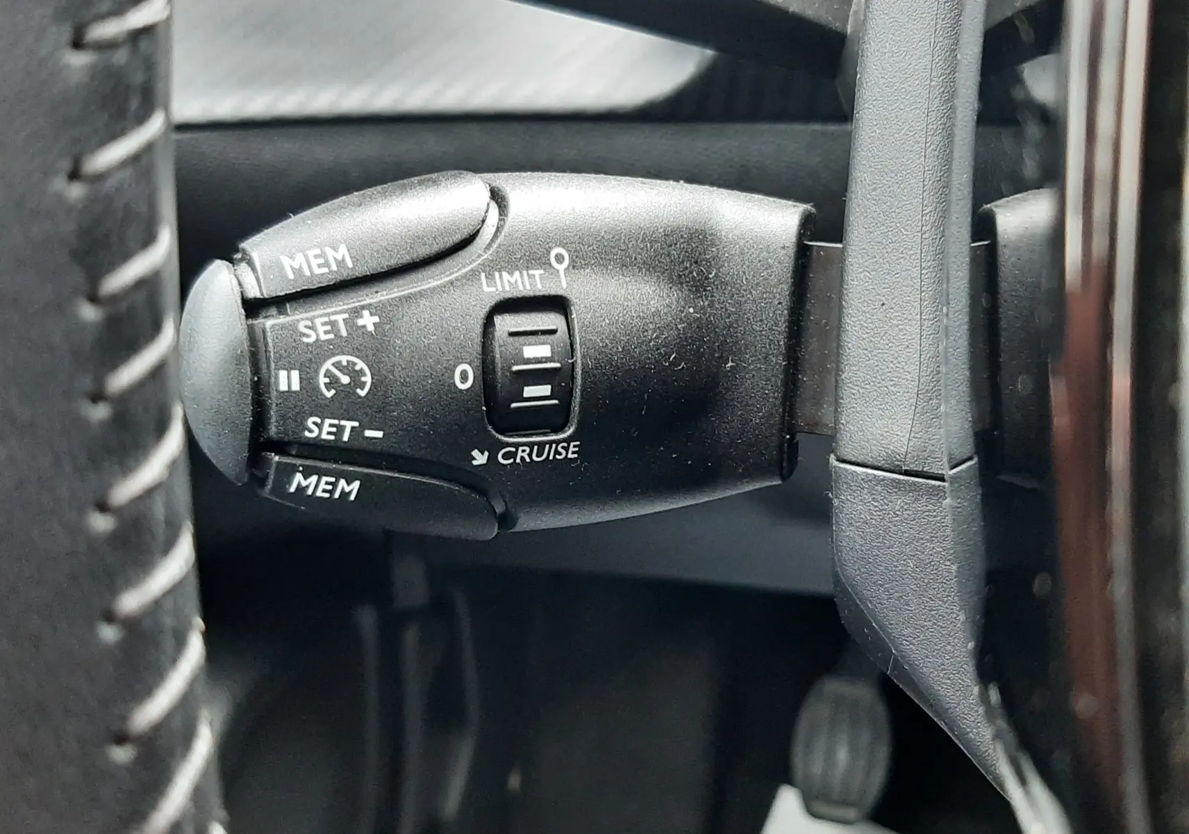 Gros plan sur la commande de régulateur de vitesse noire à gauche du volant dans une Peugeot 208 gris selenium 2024.