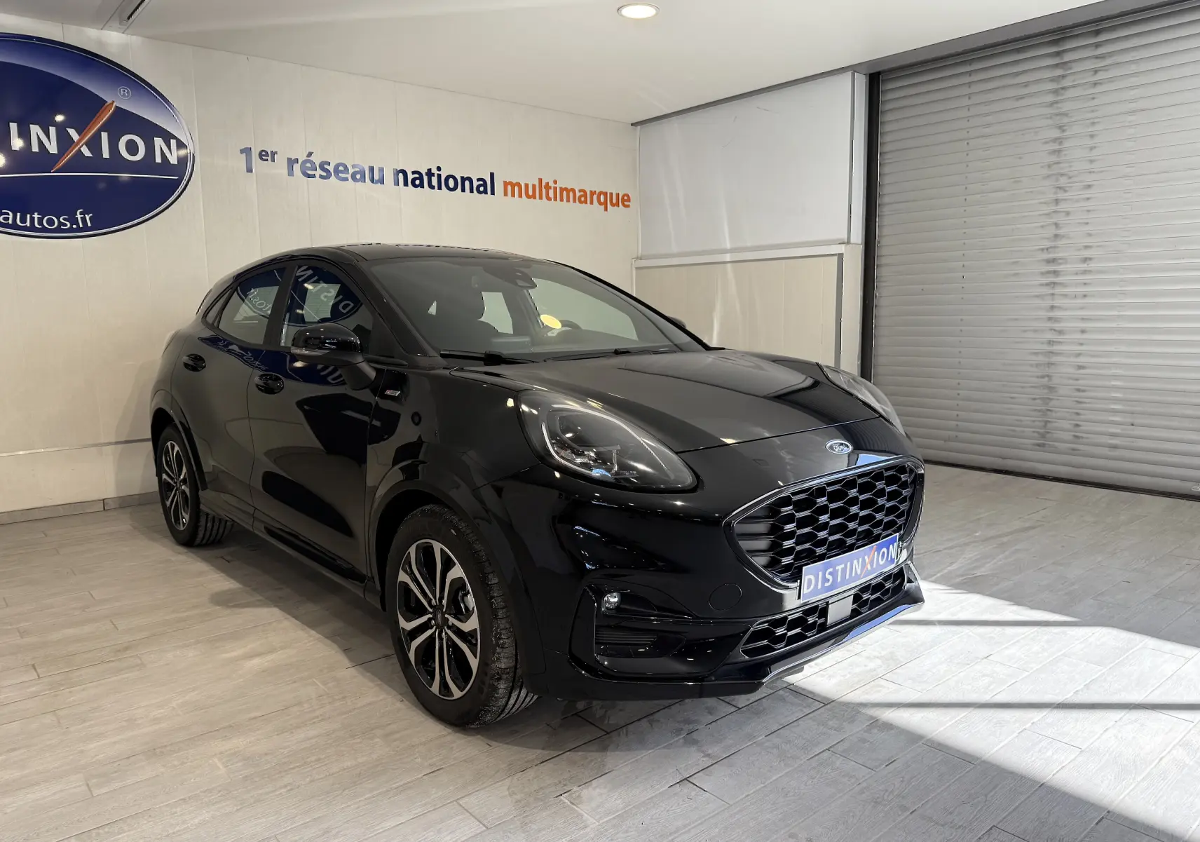 Vue 3/4 avant droit d’un Ford Puma noir Agate avec calandre imposante et jantes alliage en intérieur showroom.