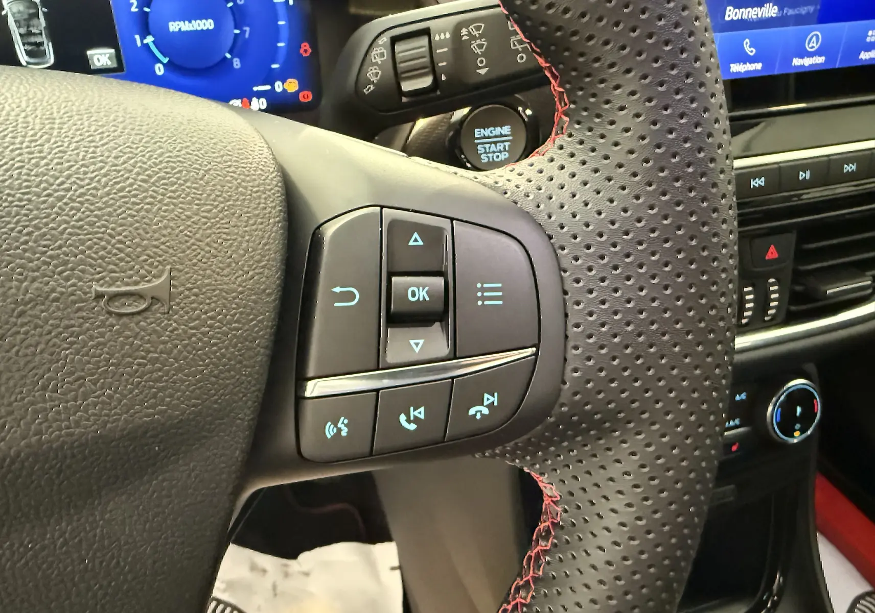 Gros plan sur le volant perforé noir avec surpiqûres rouges du Ford Puma 2022, montrant les commandes multifonctions et le bouton start-stop.