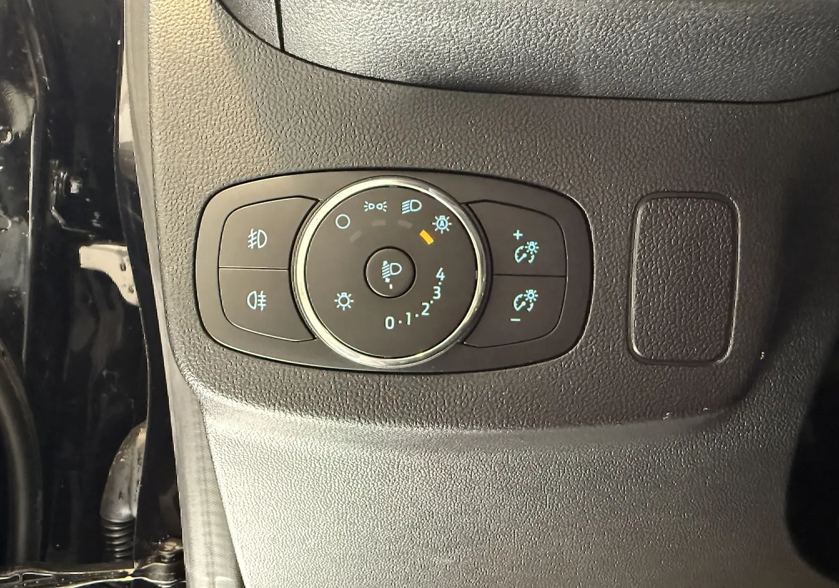 Gros plan sur le bouton de réglage des phares du Ford Puma noir agate, situé côté gauche du tableau de bord.