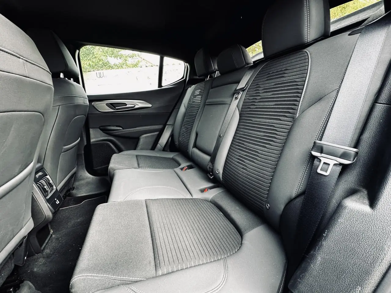 Vue intérieure côté droit de la banquette arrière noire de l'Alfa Romeo Tonale 2024 avec sellerie mixte tissu et cuir.