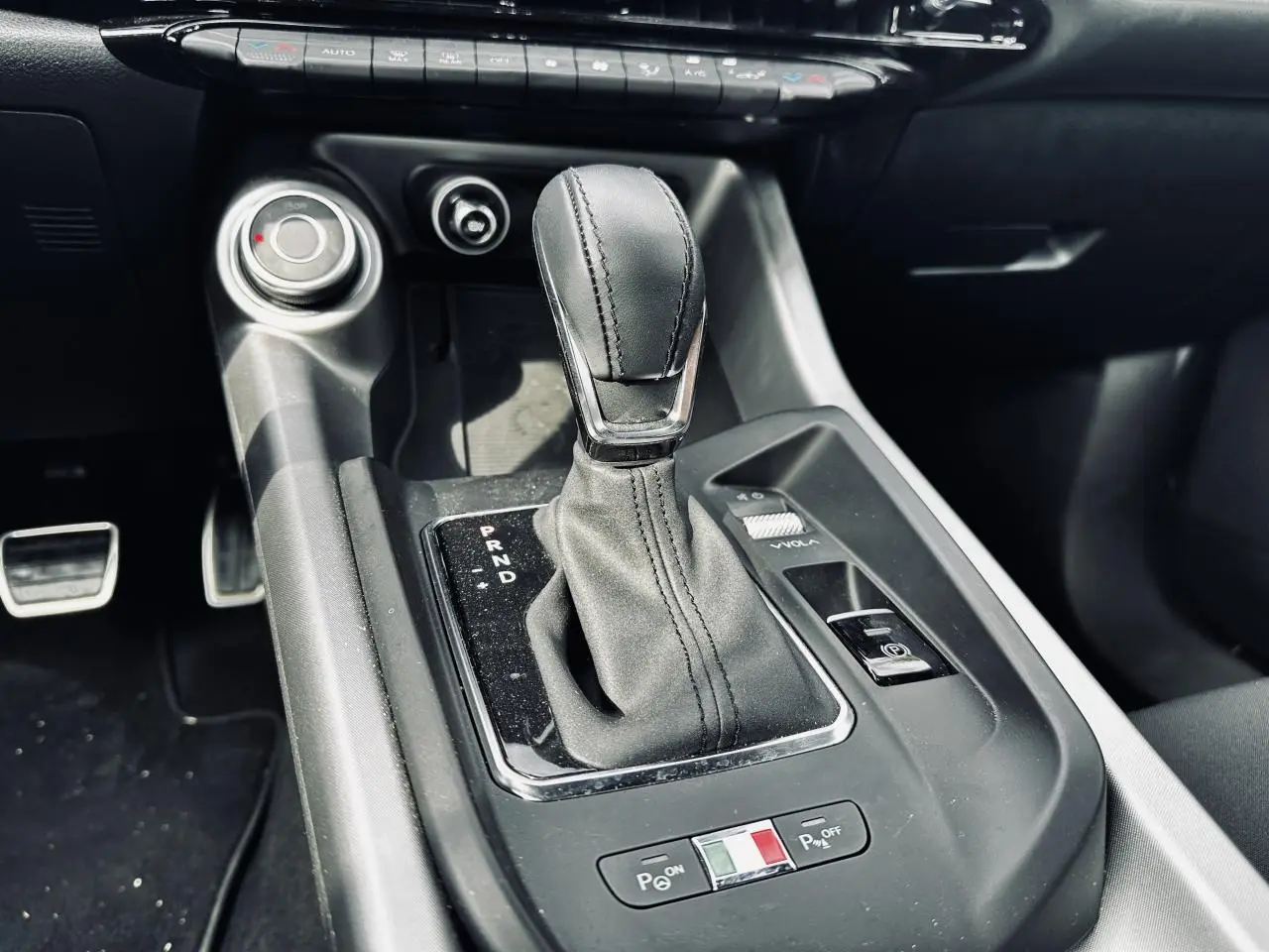 Gros plan sur la console centrale de l'Alfa Romeo Tonale 2024, avec levier de vitesse automatique et bouton de stationnement électrique.