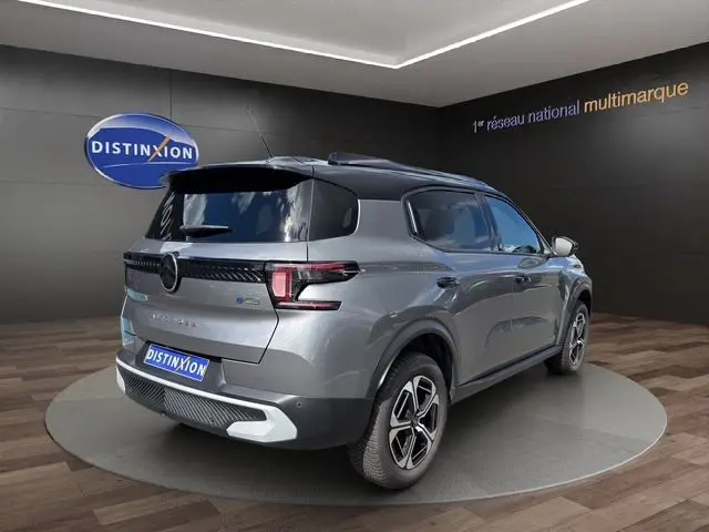 Vue 3/4 arrière droite d'un Citroën C3 Aircross électrique gris mercury avec toit noir dans un showroom.