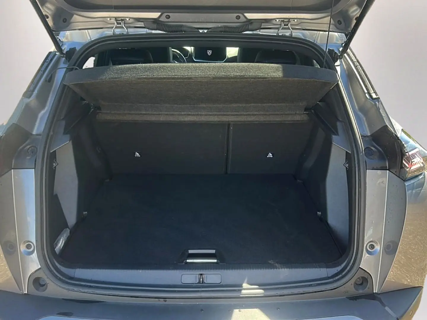 Coffre ouvert vu de l'arrière d'un Peugeot 2008 gris artense avec cache-bagages relevé et intérieur spacieux.