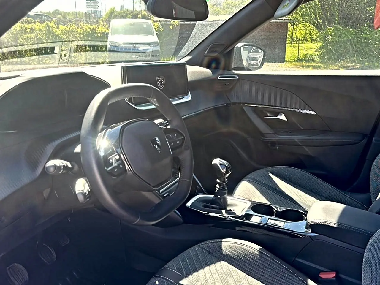 Vue intérieure côté conducteur du Peugeot 2008 1.2 100 allure 2025, volant multifonction et levier de vitesse manuel visibles.