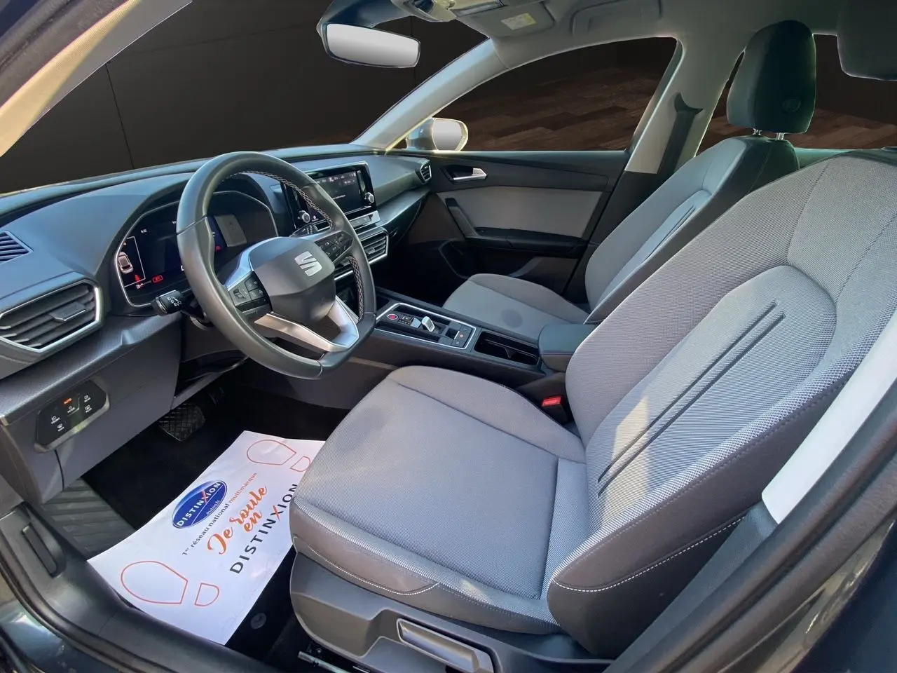 Vue intérieure côté conducteur de la SEAT Leon IV 2024 avec sièges tissu gris clair et tableau de bord moderne.