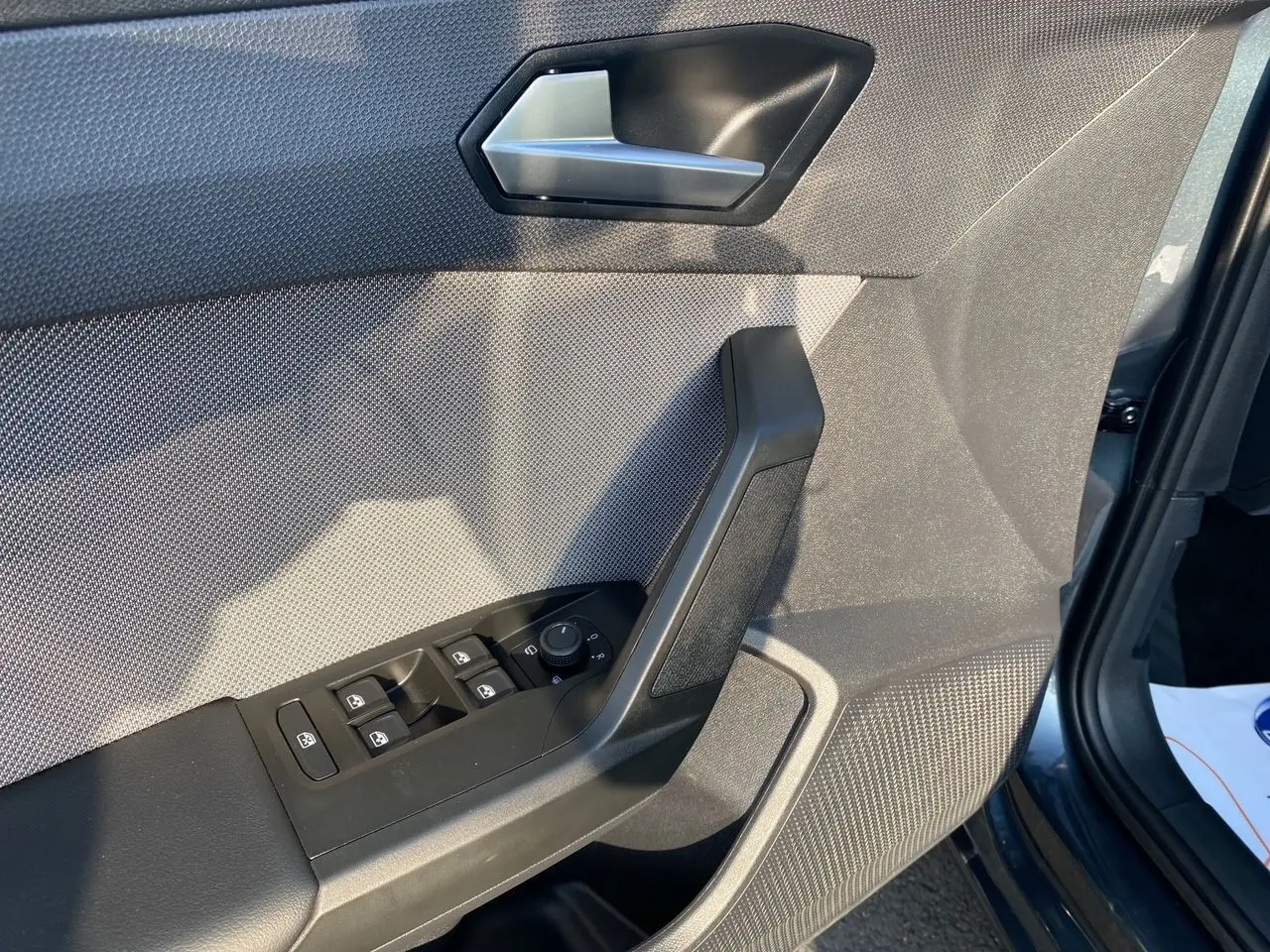 Gros plan sur la porte côté conducteur d'une SEAT Leon gris magnetic, montrant les commandes des vitres et le revêtement texturé.